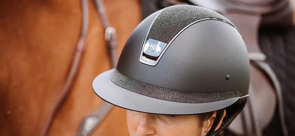 Black equestrian helmet with glittery textured stripe and silver logo plate perfect for horse riding hats collection