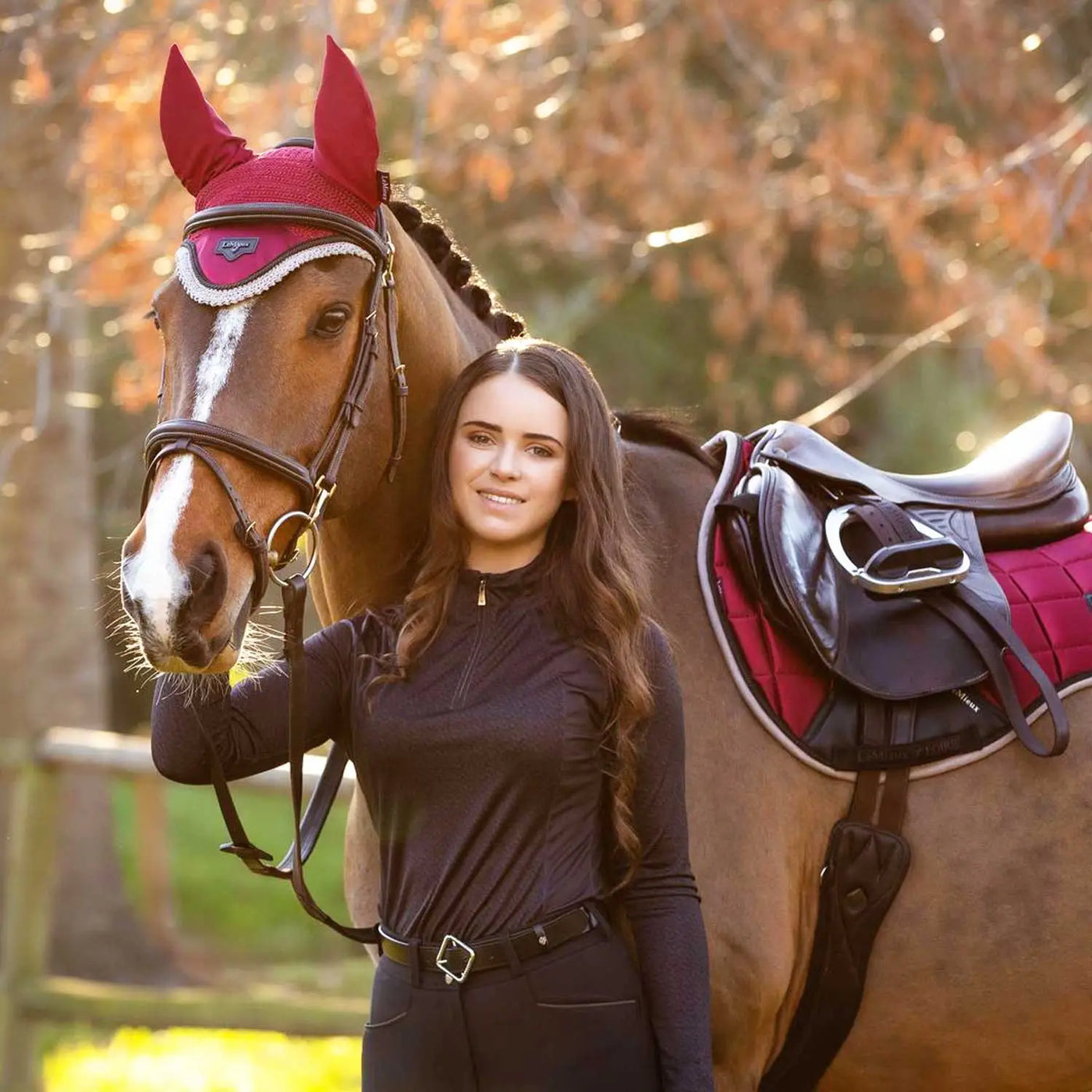 The horse wears a lemieux ember autumn red ear cover with white trim and matching saddle pad from the ember autumn colour collection