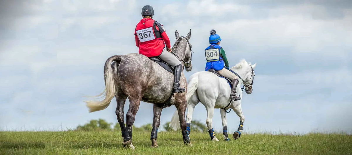 Two athletes wearing point two air jackets ride a grey dapple and white horse in competition gear