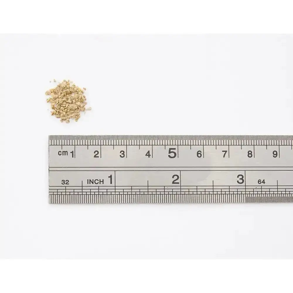 A small pile of light beige allen & page range layers crumble sits above a metallic ruler marked in centimeters and inches