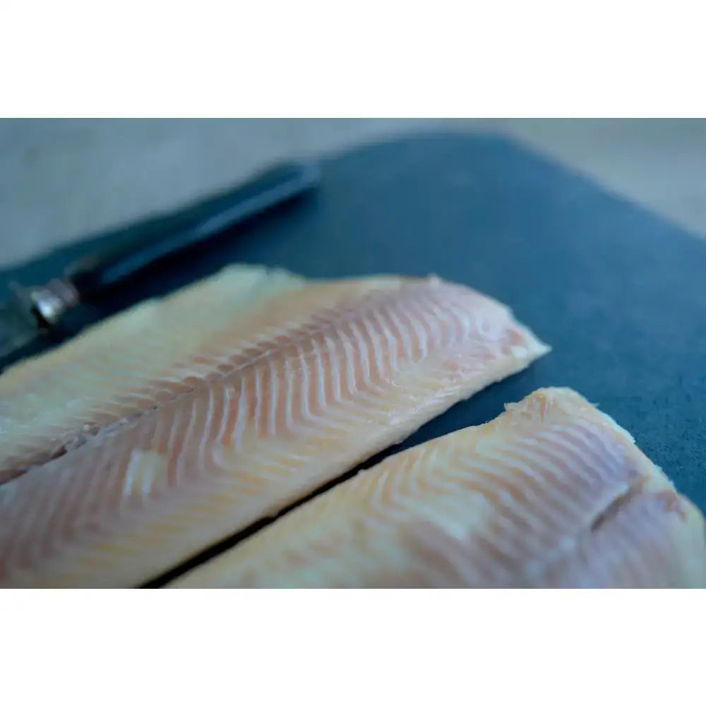 Two pale hot smoked trout fillets with visible white muscle lines from blakewell smokehouse devon on dark board
