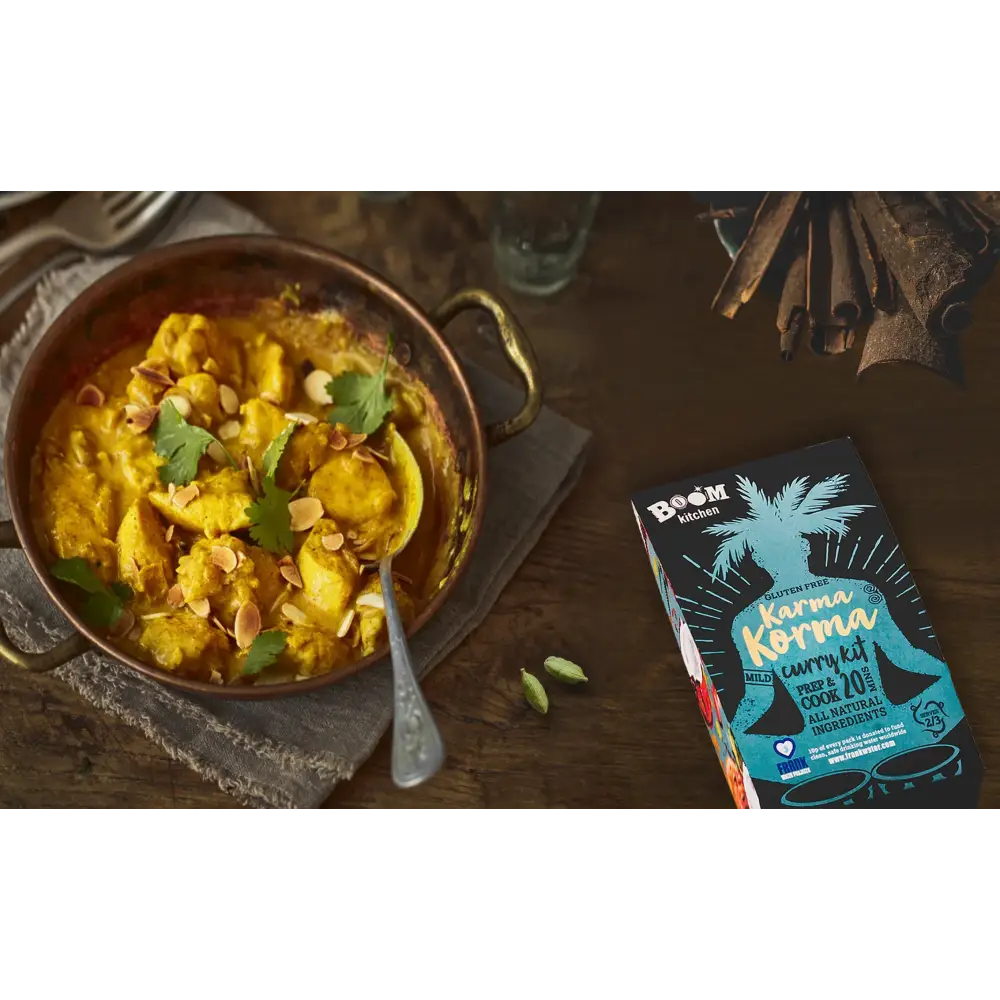 A vibrant yellow karma korma curry in a rustic copper pot garnished with cilantro and almonds from boom kitchen karma
