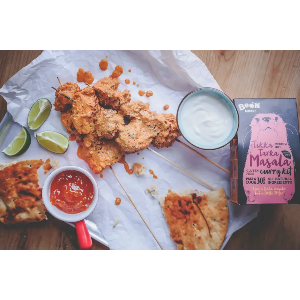 A vibrant orange boom kitchen tikka tarka curry on skewers with lime wedges yogurt dip and red-handled sauce cup