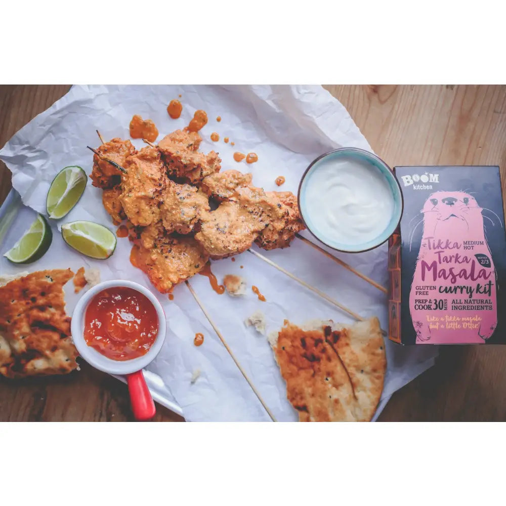 A vibrant orange boom kitchen tikka tarka curry on skewers with lime wedges yogurt dip and red-handled sauce cup