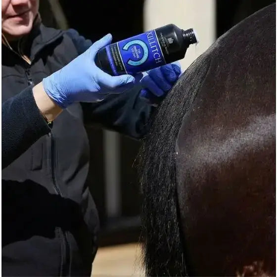 A sleek black bottle of martin killitch lotion with a blue label and silver cap held by gloved hands