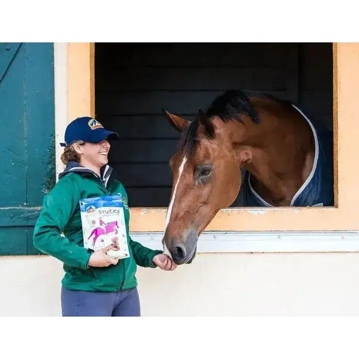 A brown horse with a white stripe wearing a blue and white blanket next to cavalor fruities healthy horse snacks 750g