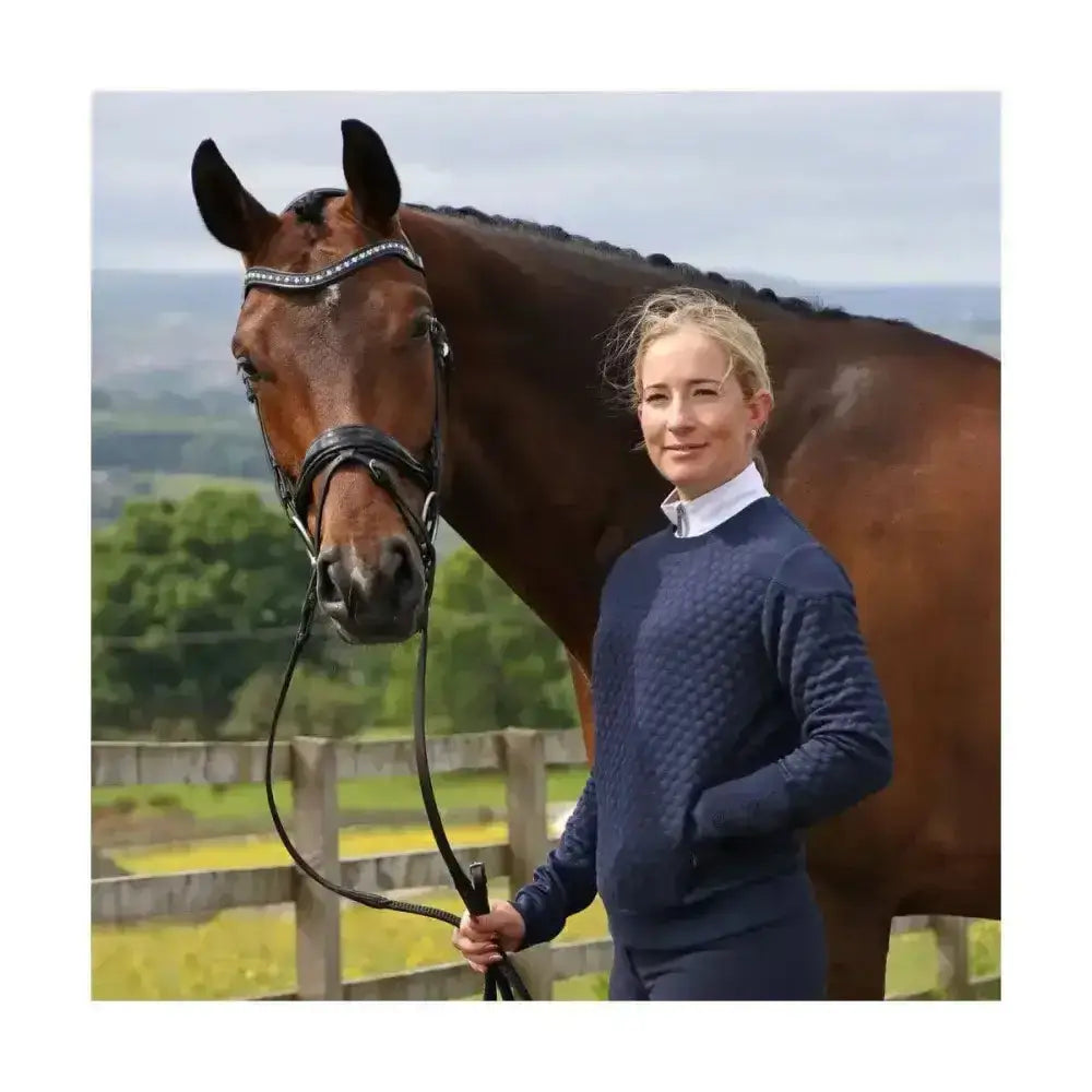A dark brown horse wearing a black bridle with rhinestones next to a coldstream foulden sweater navy with technical raised hexagonal pattern