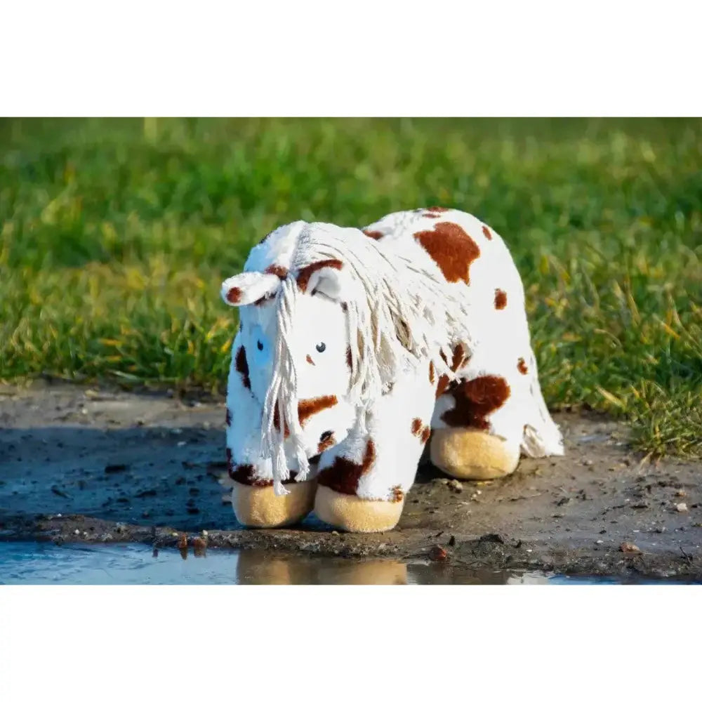 A plush crafty ponies toy pony skewbald with white and brown spots and fringed mane standing on muddy ground