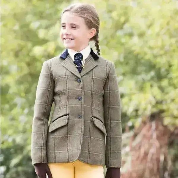 A young girl wearing an equetech stowe deluxe junior tweed riding jacket in green with plaid pattern and button closures