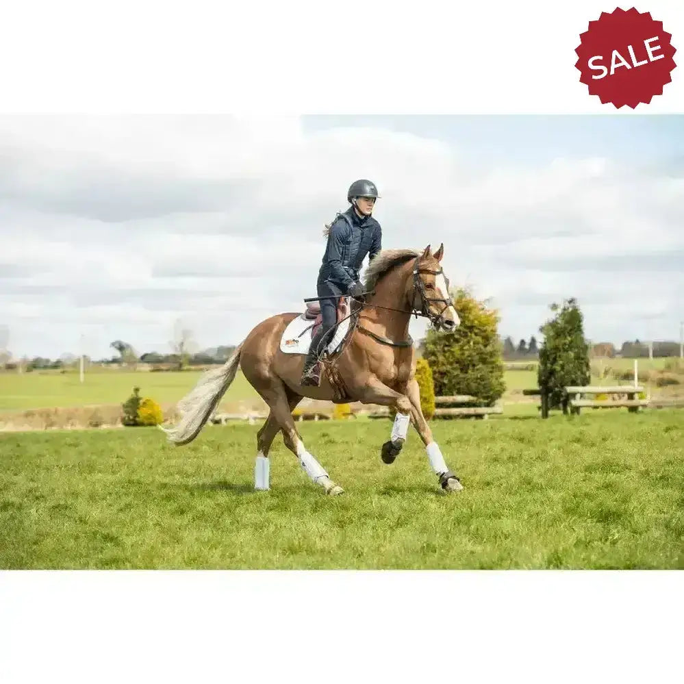 A chestnut horse gallops wearing white equilibrium tri-zone impact sports boots with protective leg wraps in a grassy field