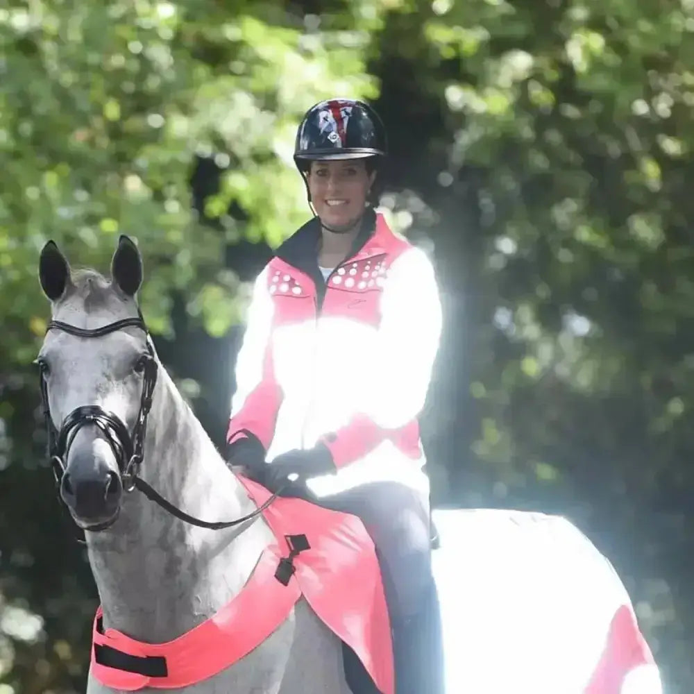 A gray horse wearing a bright pink equisafety mercury lightweight reflective riding coat with black straps and bridle