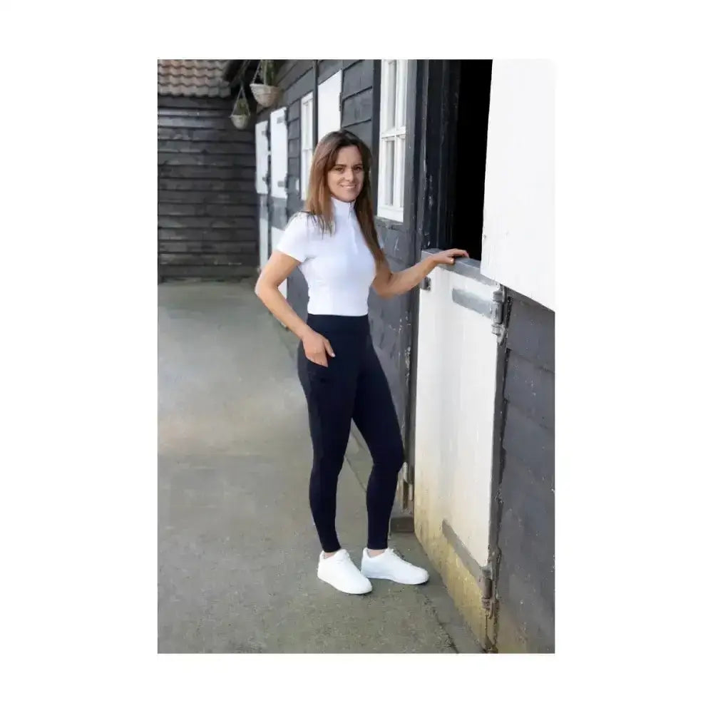 A woman wearing hy equestrian children’s melton riding tights in black with white short-sleeved turtleneck top