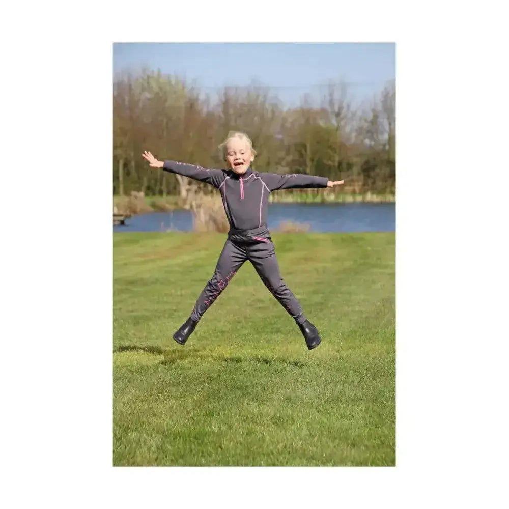 A young child mid-jump wearing a dark gray equestrian stella funky base layer with pink zippers outdoors