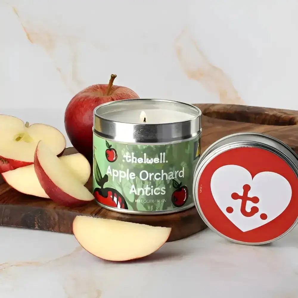 A lit green-labeled apple orchard antics thelwell collection candle in a silver tin with a red heart lid by hy equestrian