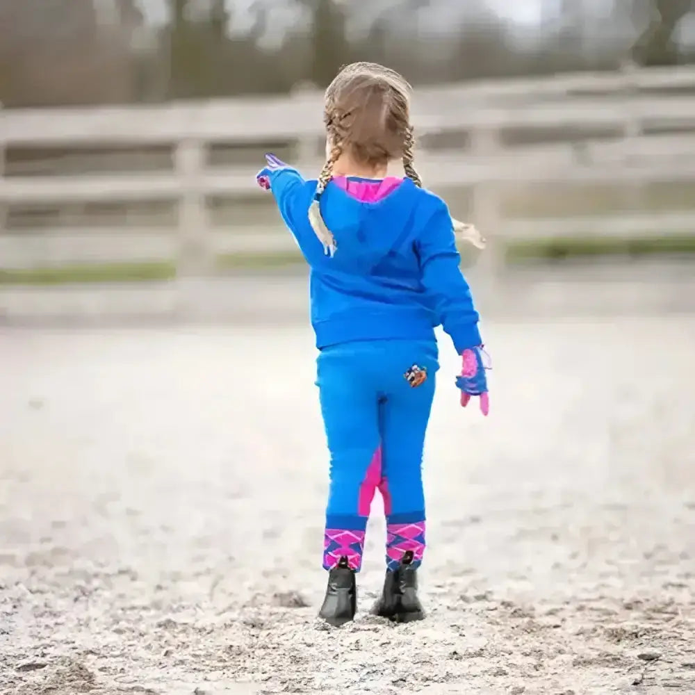 A young girl in a vibrant blue fleece tots jodhpurs with pink accents from the hy equestrian thelwell collection stands outdoors