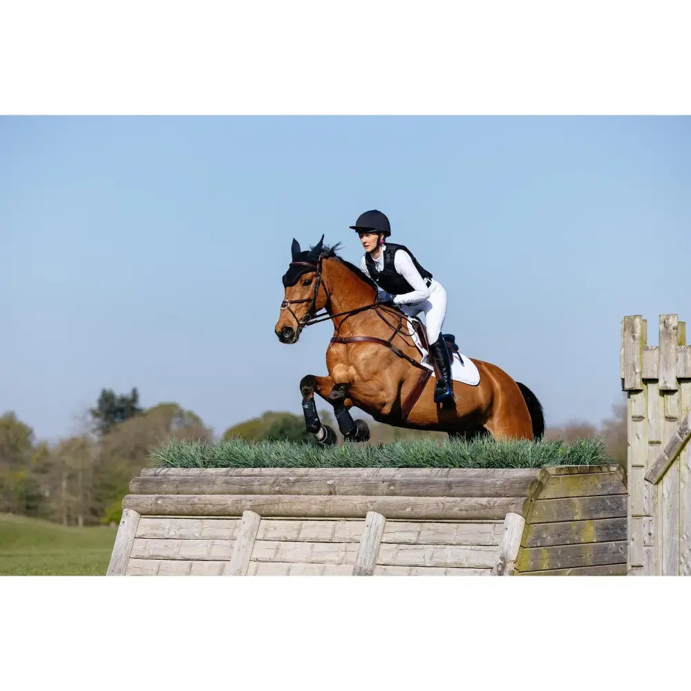 A brown horse mid-jump wearing a black bridle and lemieux 3d mesh eurojump square white fabric weave saddle pad