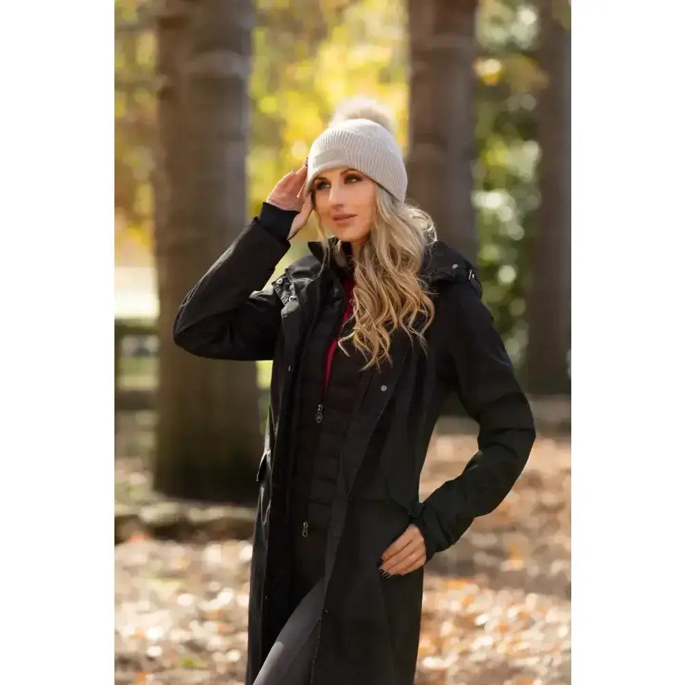 A light gray knitted beanie with a fluffy pom pom paired with lemieux amelie waterproof lightweight riding coat black
