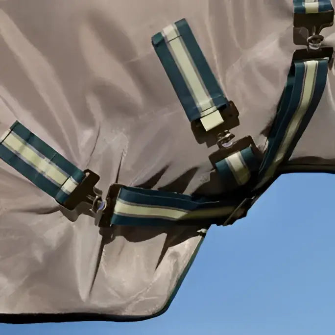Blue and white striped fabric straps with black buckles on beige lemieux arika camo shower-tek fly rug jungle horse blanket