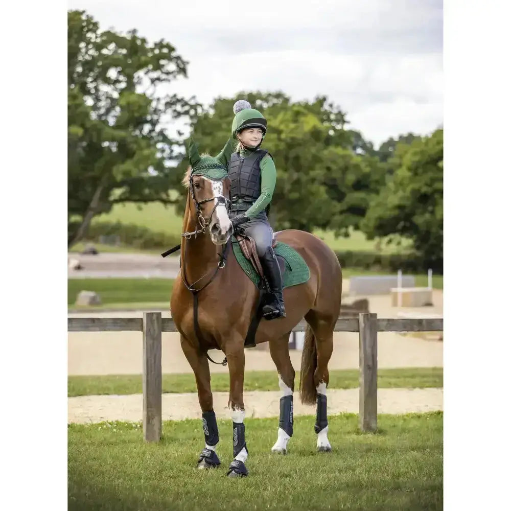 A young rider wearing lemieux base layers hunter green sits on a brown horse with matching protective leg wraps
