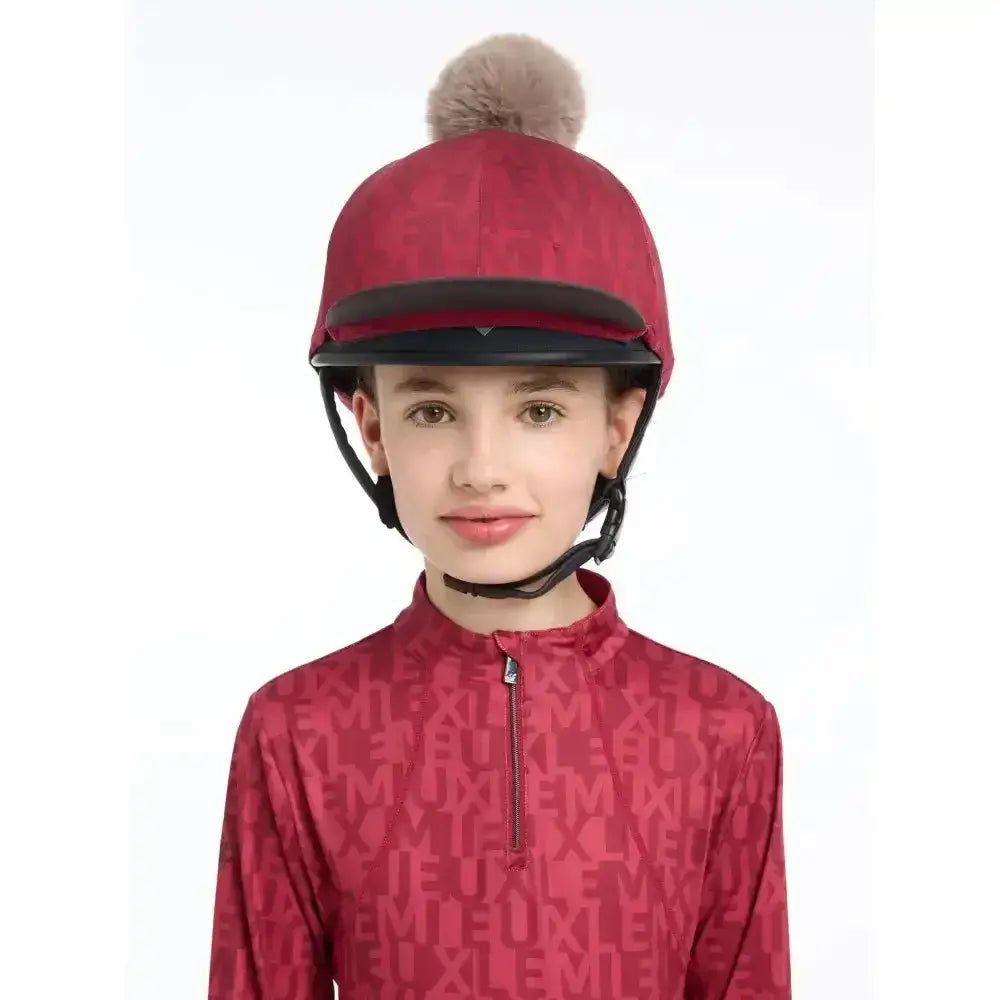 Lemieux casey hat silk ember is a red jockey helmet with a black visor and a fluffy beige pom-pom on top