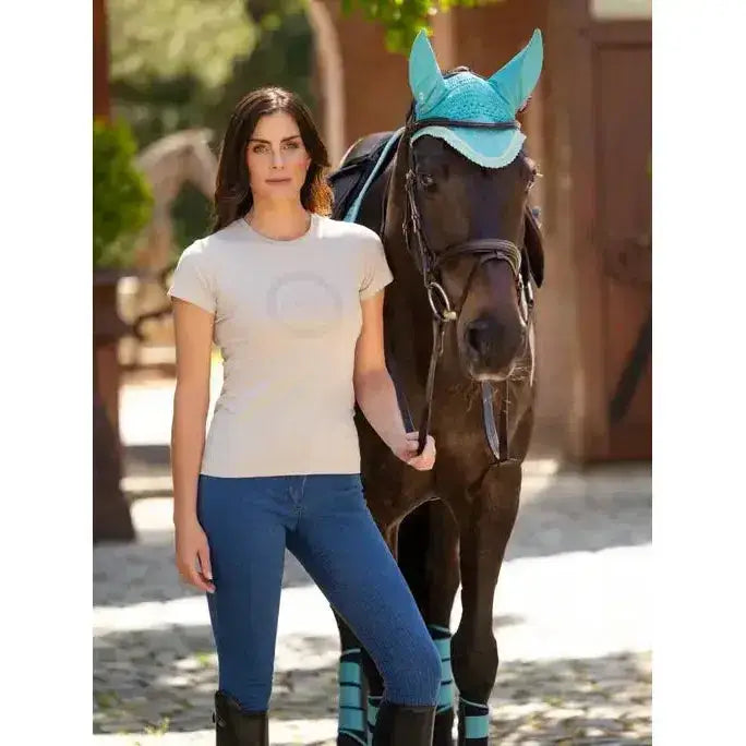 A woman stands beside a horse wearing a lemieux classique stone t-shirt in light gray with a subtle logo and blue riding pants