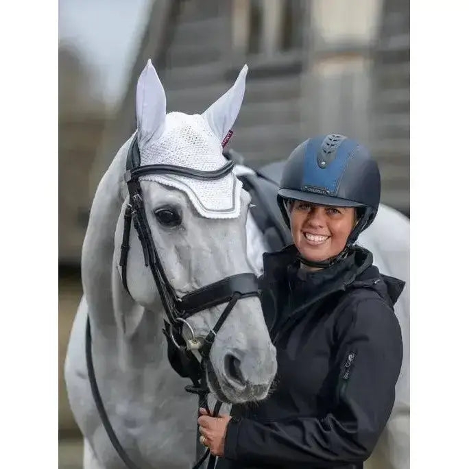 Gray horse wearing a white mesh lemieux crystal fly hood with intricate four-way pattern and black bridle