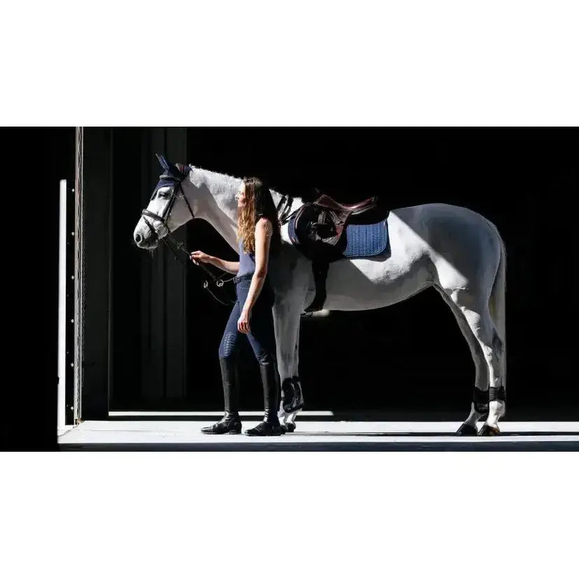 A sleek white horse wearing a lemieux finesse eurojump faux leather saddle pad in navy eurojump square navy