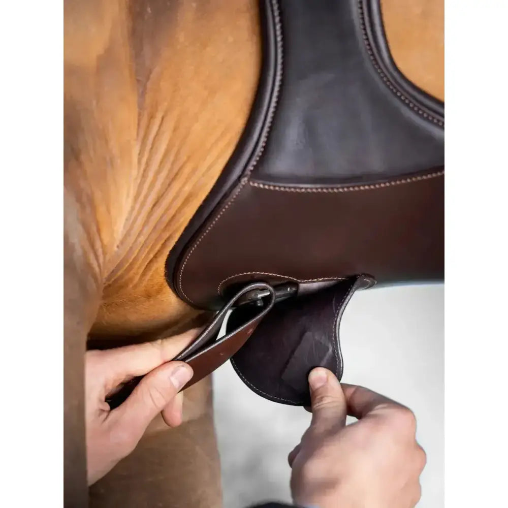 Brown leather lemieux gel-tek anatomic long stud girth with stitched edges and dark brown flap being adjusted by hands