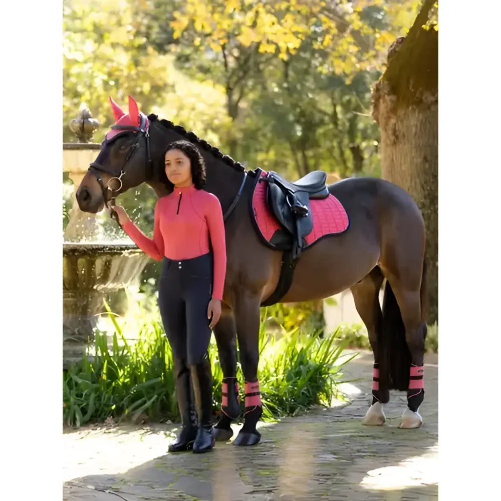 A dark brown horse wearing lemieux grafter brushing boots cranberry pink hoof boots and matching saddle pad and headpiece