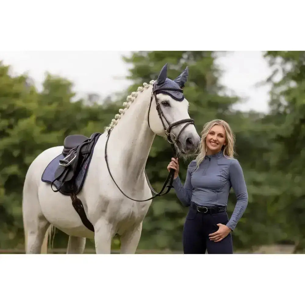 A white horse wearing a dark blue bridle with pearl details showcasing the lemieux ladies base layer jay blue product