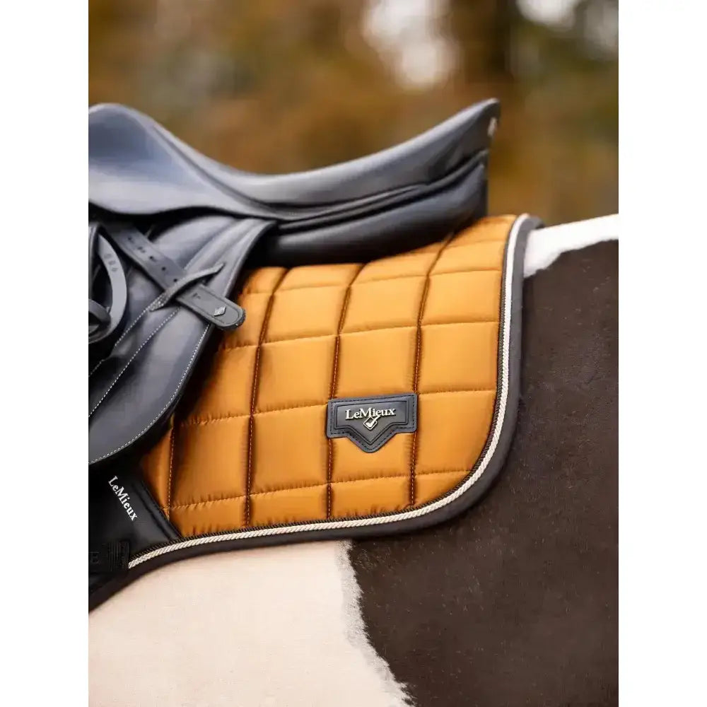 A quilted mustard-yellow saddle pad with black trim and lemieux loire classic patch featuring diamond stitching
