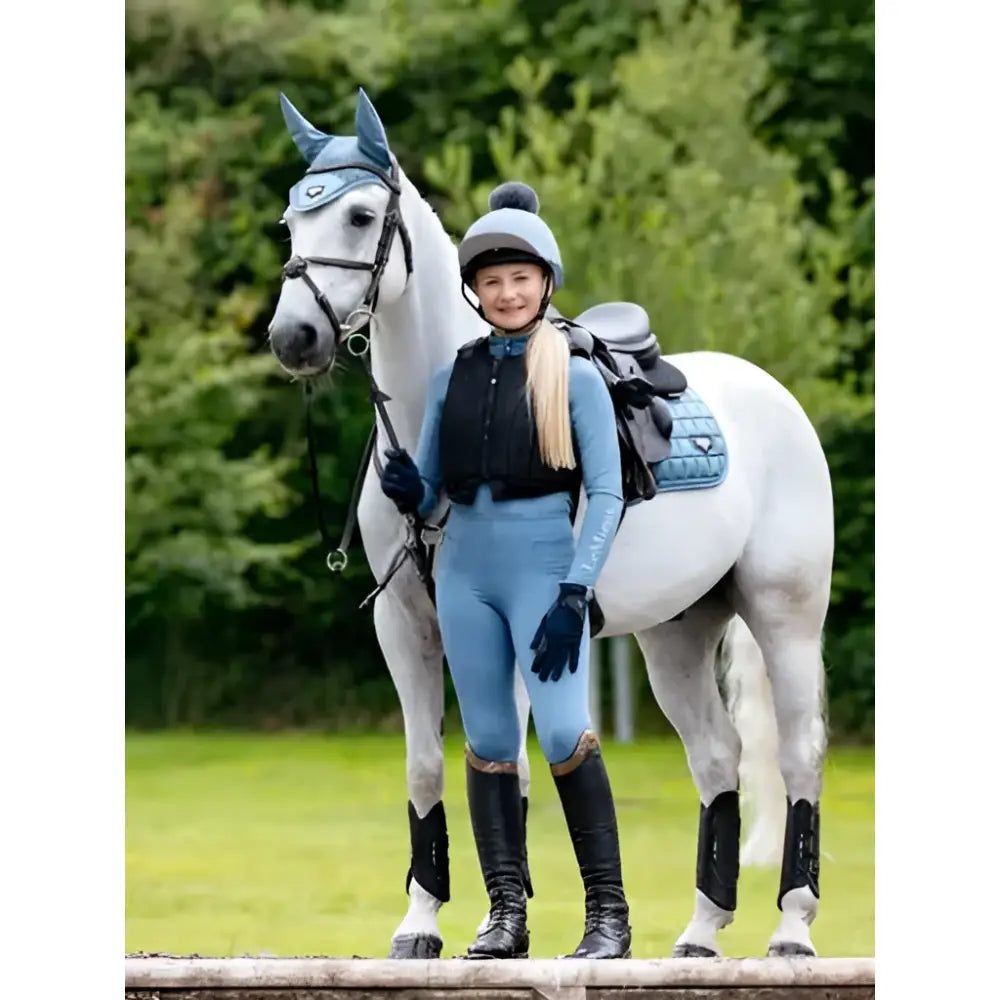 A white horse wearing lemieux loire classic square ice blue protective gear with a rider in matching blue attire