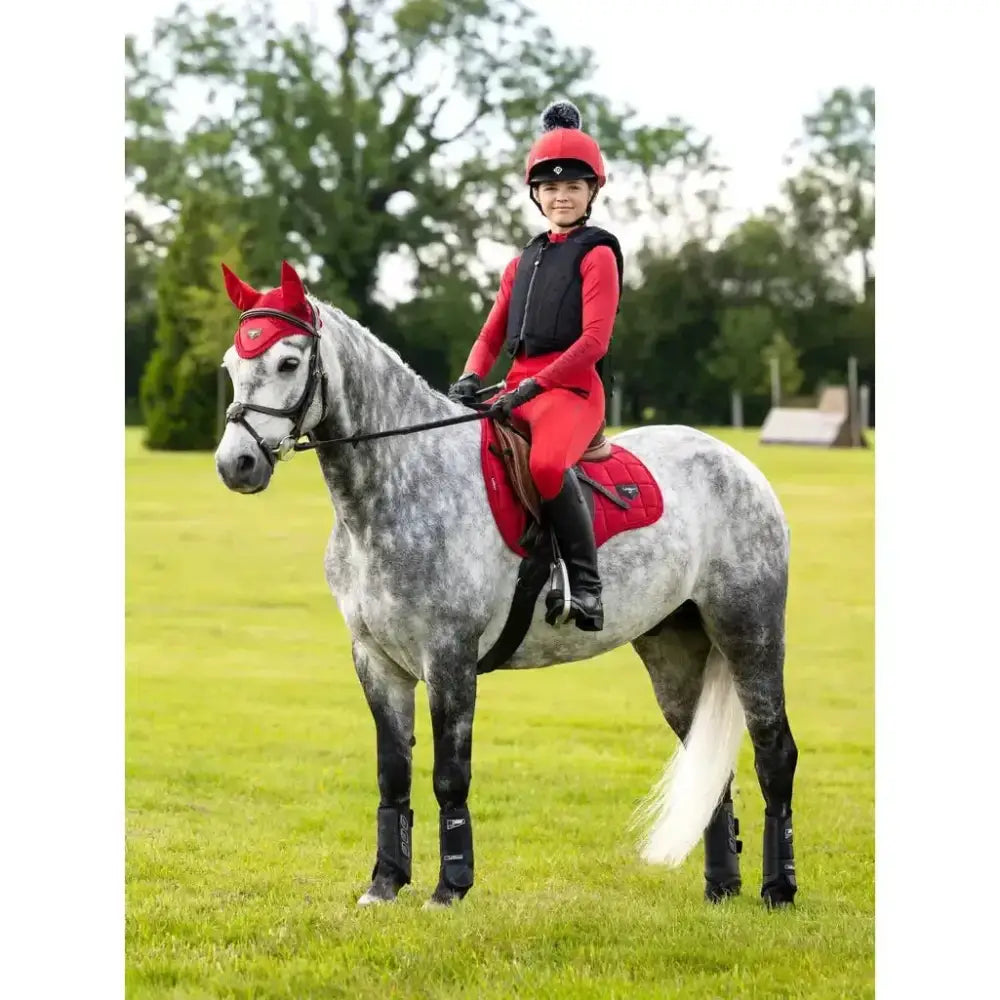A young rider sits on a grey dapple horse wearing the red leMieux Loire range saddle pad made of woven satin fabric
