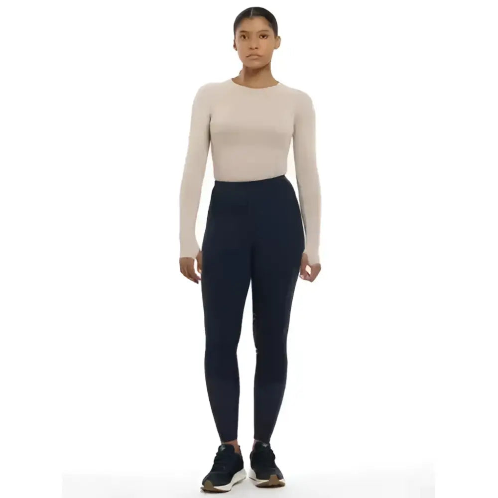 A woman wearing lemieux lydia mesh leggings navy with a beige top and black athletic shoes for an active look
