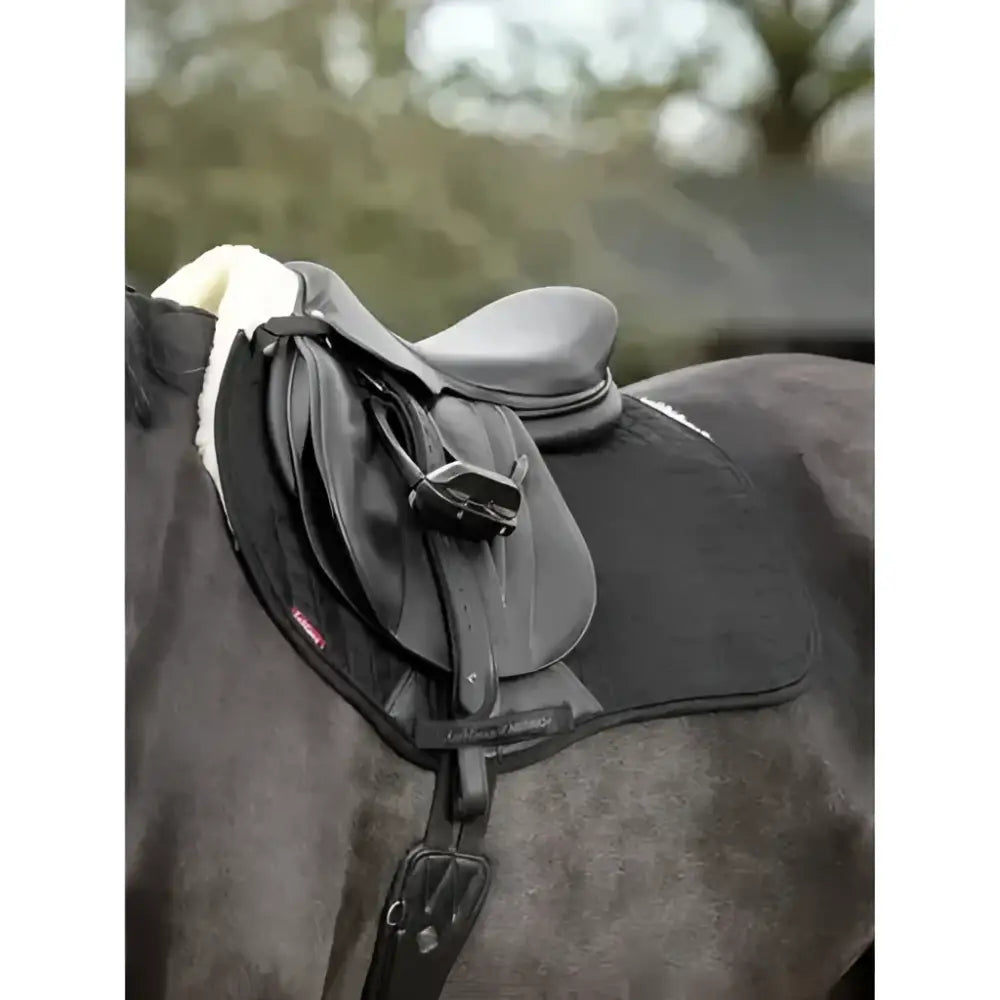 Black leather lined suede eurojump square saddle with white fleece resting on a dark horse by LeMieux