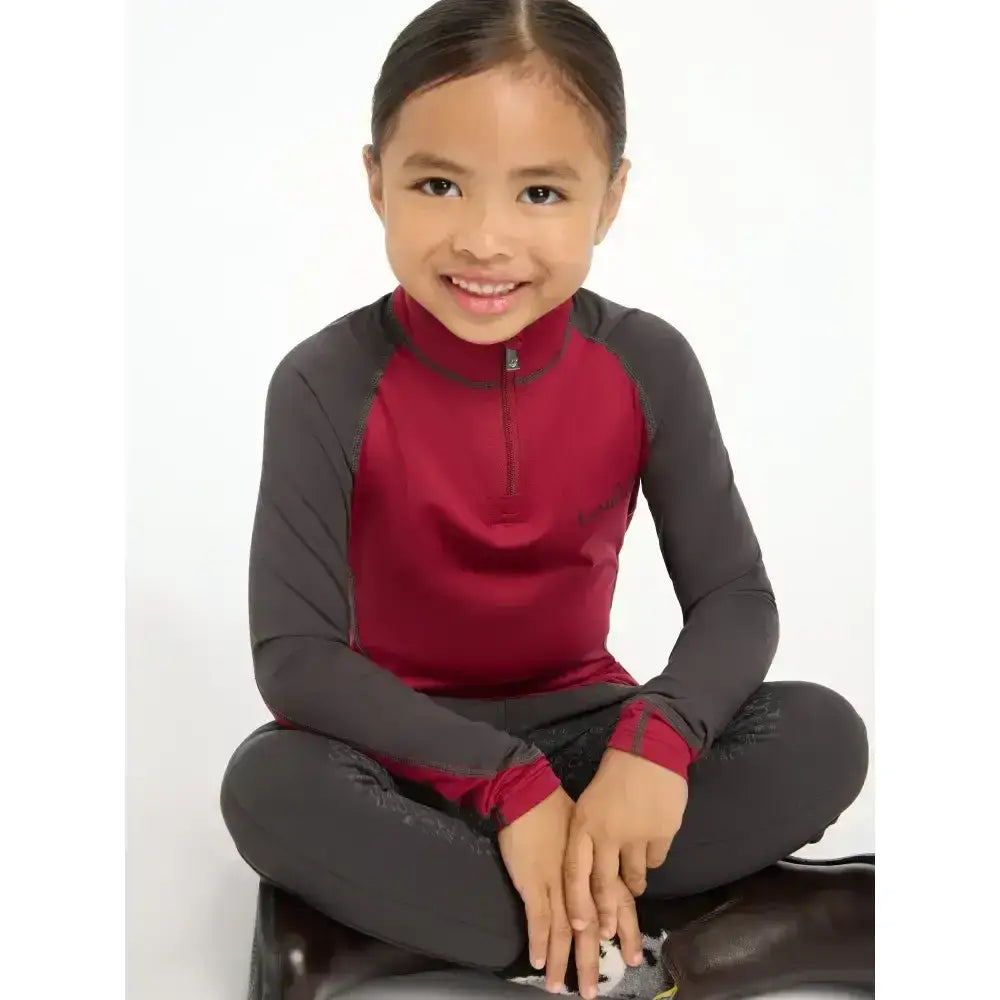 A young girl wearing a maroon and gray lemieux mini base layer ember with a half zip for mini riders running