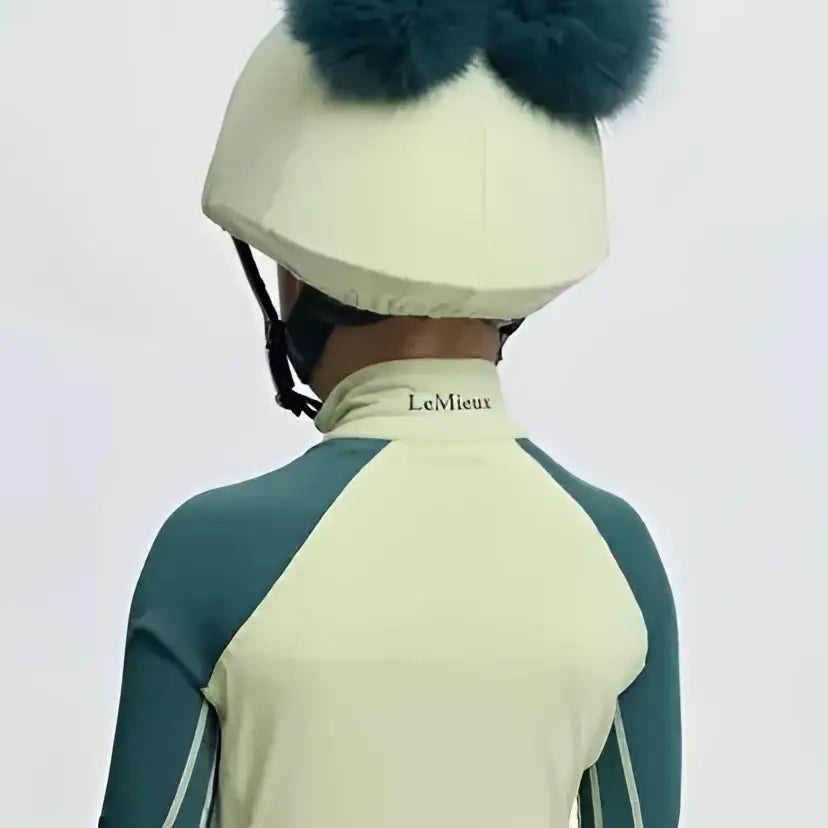 Cream-colored lemieux mini equestrian helmet with dark teal faux fur pom-poms silk macaron style