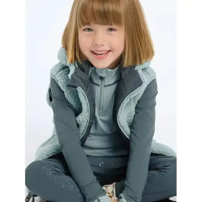 A child wearing a dark gray lemieux mini elsie reversible gilet petrol with light blue sherpa trim and fleece lining