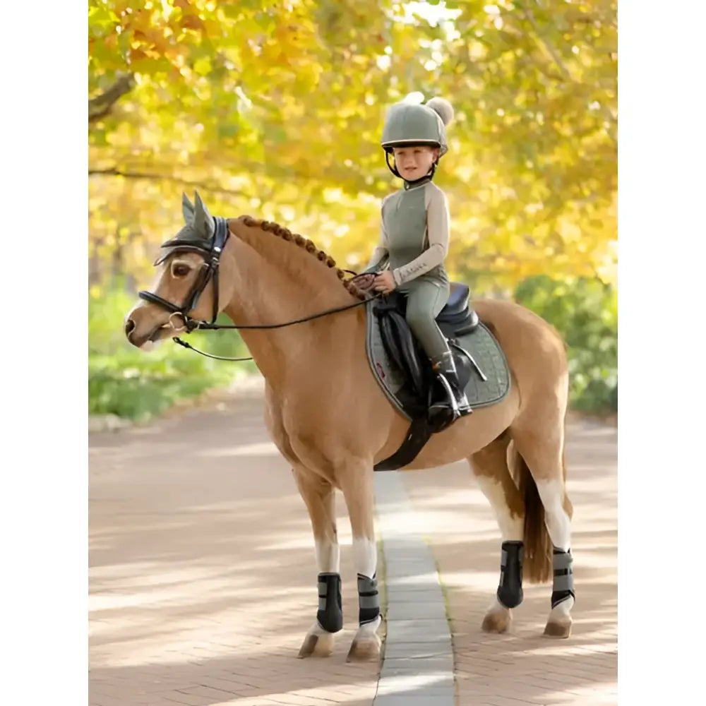 A young rider wearing a gray equestrian helmet rides a chestnut horse with lemieux mini grafter brushing boots rosemary