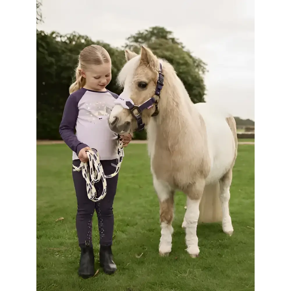 A young girl wearing a lemieux mini jamie lemon long sleeve top lilac stands next to a cream pony