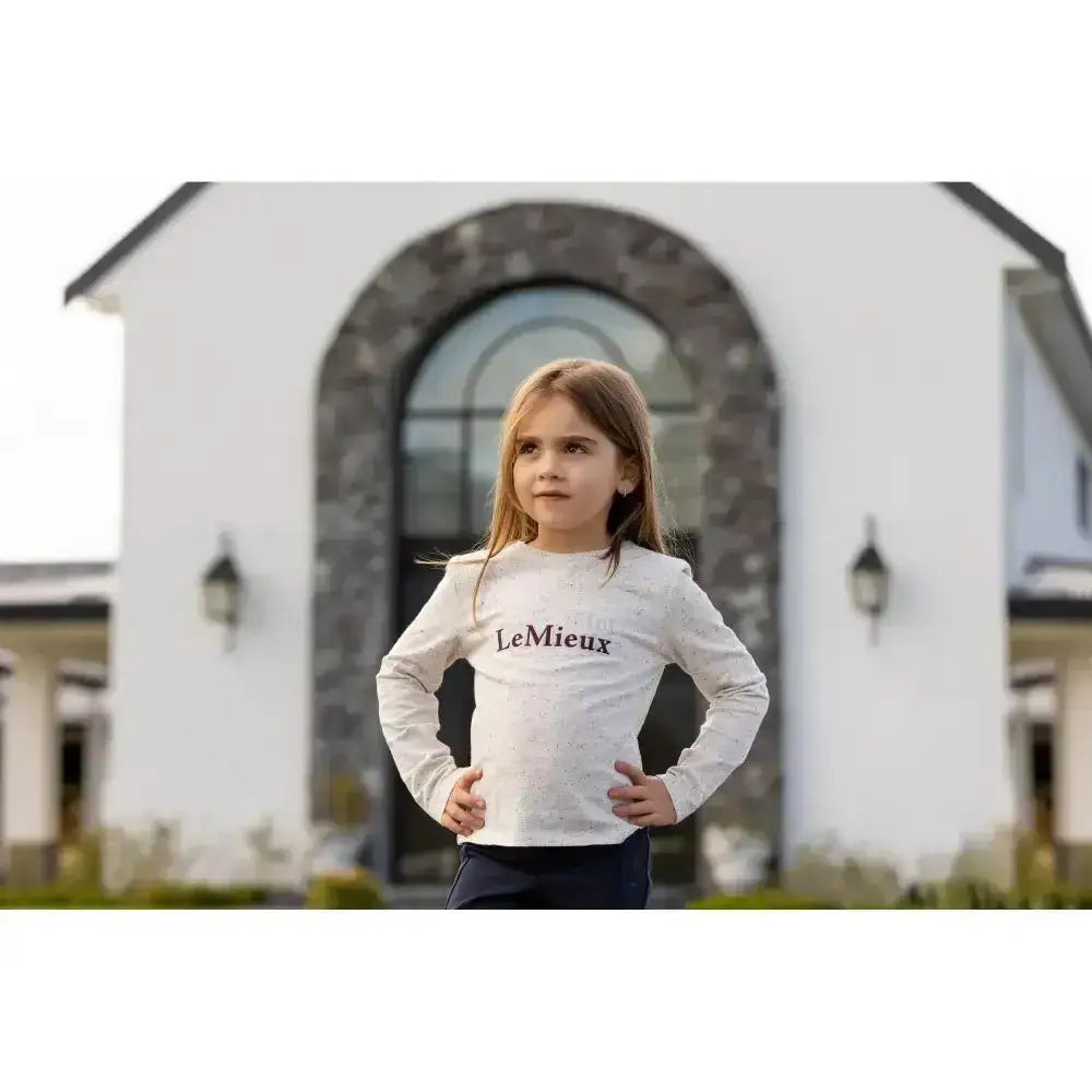A child wearing a lemieux mini jessie long sleeve top in ecru with black print on a white shirt