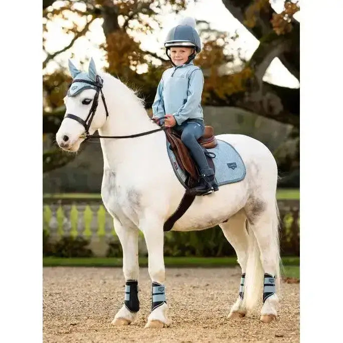 A young rider wears a lemieux mini mari micro fleece glacier jacket while sitting on a white horse with matching blue gear