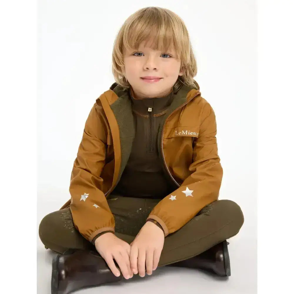 A child wearing a mustard-yellow lemieux mini milo winter puffer jacket with white stars and olive lining
