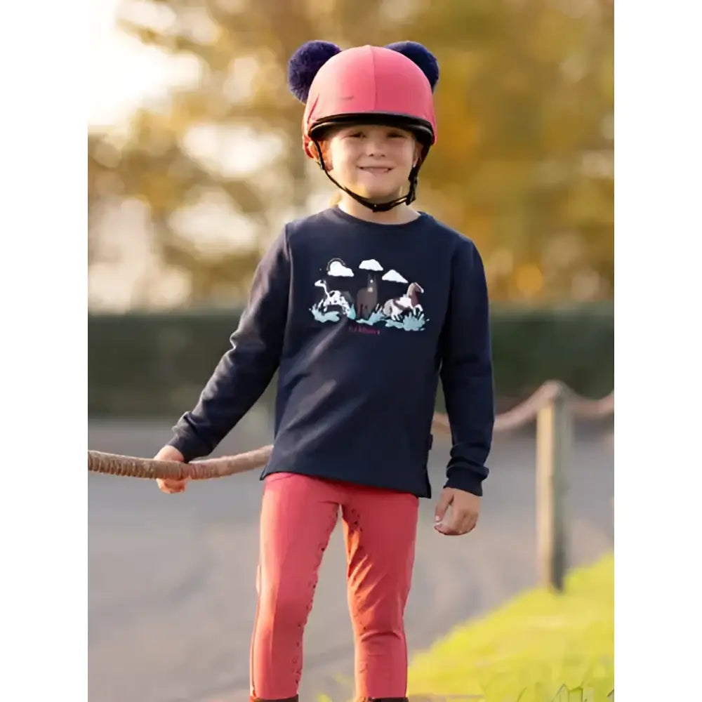 Pink helmet with black pom poms paired with lemieux mini poppy long sleeve top navy for stylish riding gear
