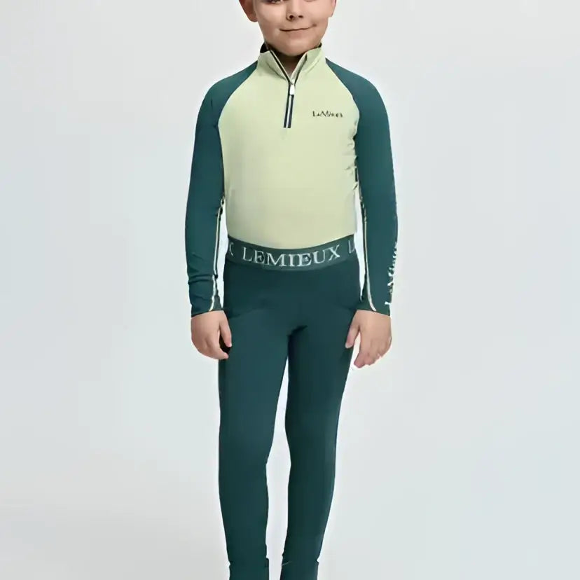 A child wearing a lemieux mini pull long-sleeved riding top with pale green torso and dark teal sleeves and leggings