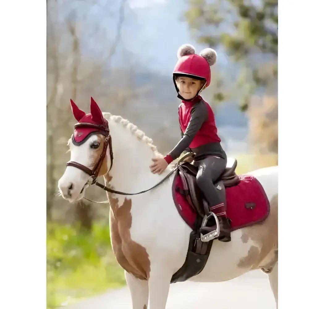 A young rider in a red helmet rides a pinto horse wearing lemieux mini pull ons cinder active riders red gear