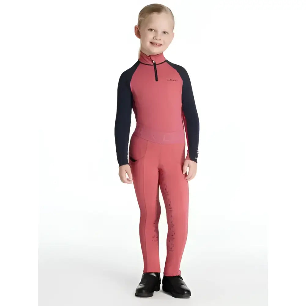A child wearing coral and black lemieux mini pull ons cranberry long sleeve riding suit with subtle leg patterns