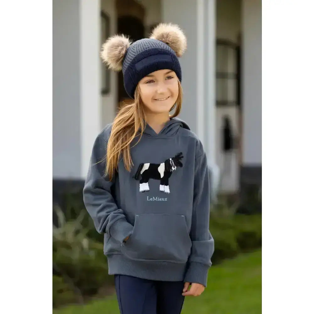 Gray lemieux mini romi hoodie petrol with black and white cow graphic paired with navy beanie with beige pom poms