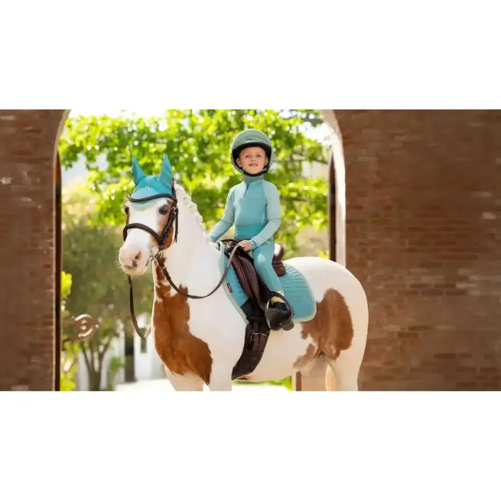 A child riding a pinto horse with teal lemieux mini suede close contact square lagoon saddle pad and matching gear