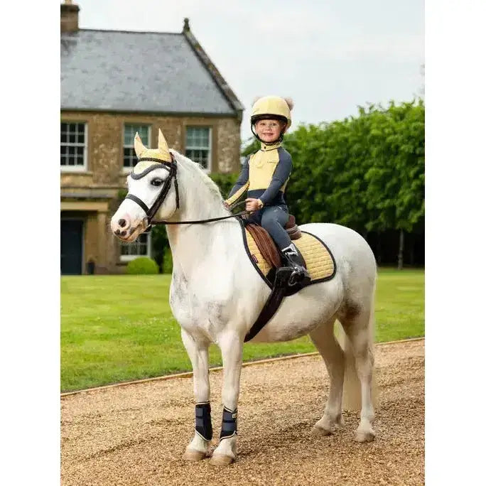 A young child rides a white horse with a lemieux mini suede close contact square mimosa saddle pad in tan
